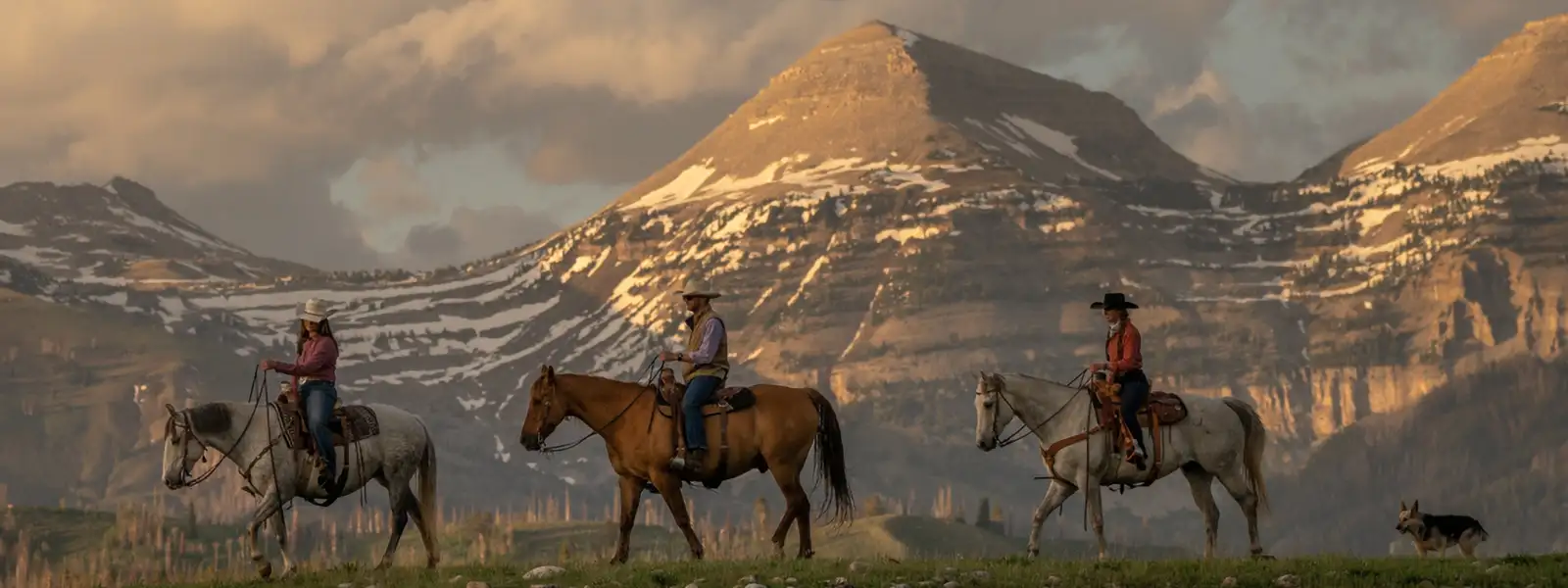 Three people riding on horseback as their dog follows in the Gros Ventre wilderness.